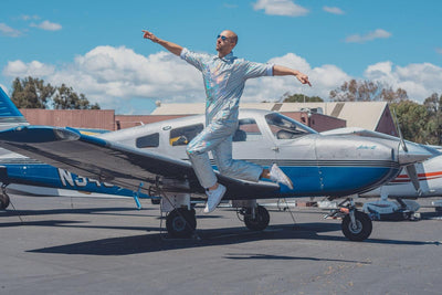 Man with airplane jumping into the air wearing holographic silver flight suit from Love Khaos festival clothing brand.