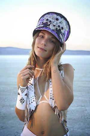 A woman wearing a white studded leather cuff, festival hat and burning man outfit from Love Khaos festival clothing brand.