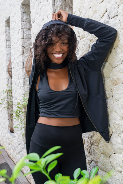 Happy woman wearing black hoodie sweatshirt, black v neck crop top and high waisted leggings from Ekoluxe sustainable loungewear brand.