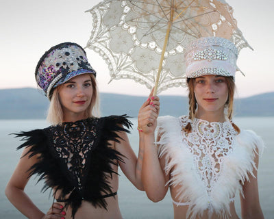 Two women at a music festival wearing feather festival bralettes and Burning Man hats from Love Khaos festival clothing brand.