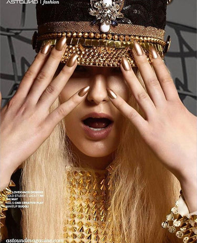 Woman with gold fingernails wears black and gold festival hat from Love Khaos festival clothing brand for Astound Magazine.