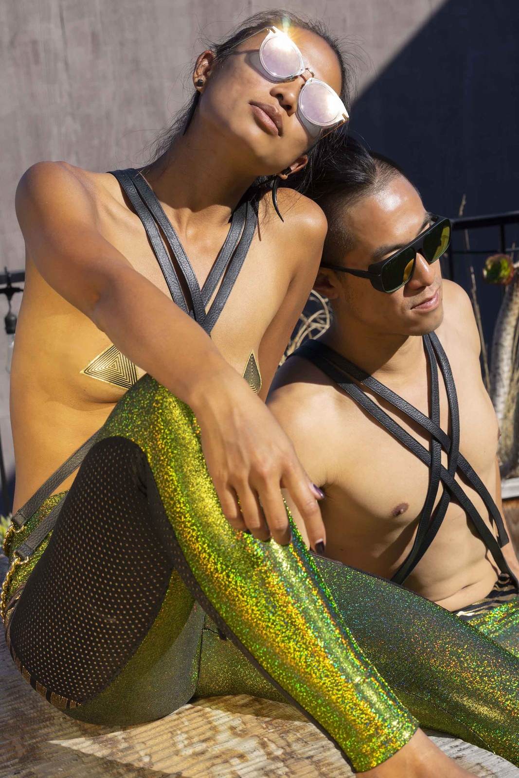 Gender fluid couple wearing unisex leather body harness with body chains and holographic leggings from Love Khaos Festival Clothing Brand